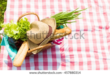 Picnic basket full of food and drinks on checkered tablecloth, top view