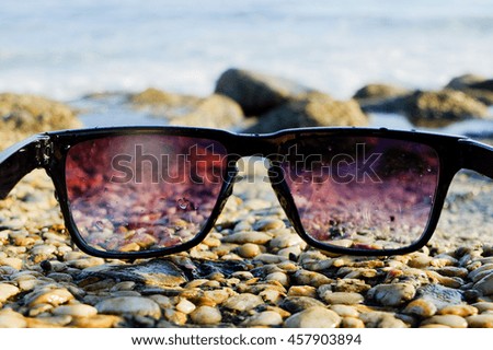 Black sunglasses lying on rocks near the sea, close up, summertime.