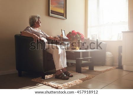 Senior woman sitting alone on a chair at home. Retired woman relaxing in living room. Royalty-Free Stock Photo #457918912