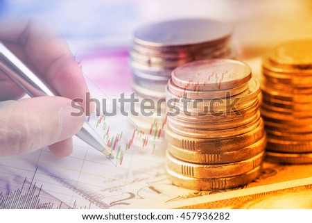 Closeup view : Stack of coins and a hand holding a ballpoint pen is examining a technical chart of financial instrument. An idea / concept of currency trading, making a decision for an optimal gain. Royalty-Free Stock Photo #457936282
