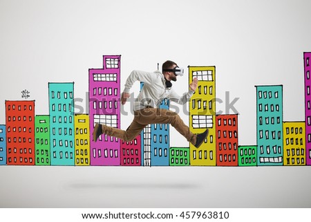 Young bearded man in virtual reality headset is photographed in mid-air jump isolated over white background with colorful buildings drawn on it