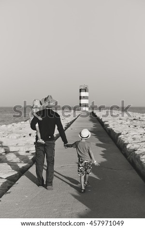 Black and white back view of male with kids walking to the red lighthouse, sunny outdoors background. Book cover design