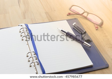 Businessman write a short note on opened notebook on wooden background with pen, glasses. warm tone.