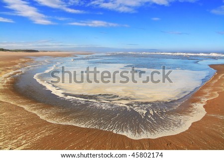 little bay and blue sky with clouds under the sandy seashore