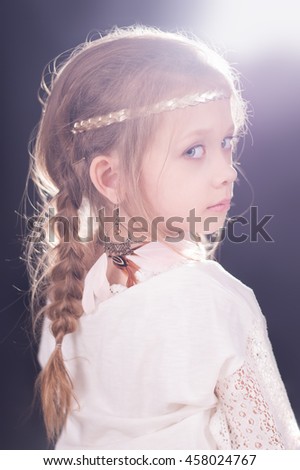 Beautiful serious expressive girl with creative braids hair style and feather boho indean accessories portrait on black background, backlight