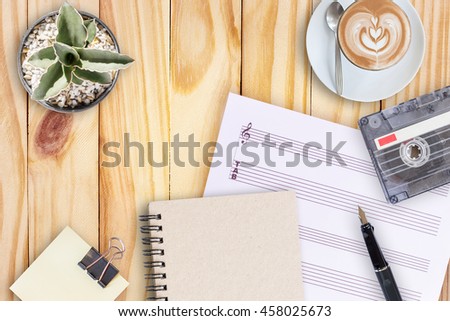 Sheet music, cactus, fountain pen, tape cassette and coffee latte on wooden table, flat lay