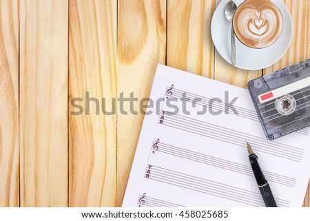 Sheet music, fountain pen, tape cassette and coffee latte on wooden table, flat lay