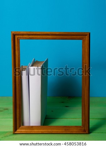 Stack of White books in brown wooden frame on a blue background on a green wooden table, free copy space, no labels, blank spine. Back to school