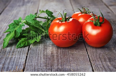 whole red tomatoes and tomatoes green leaves on wooden table Royalty-Free Stock Photo #458055262