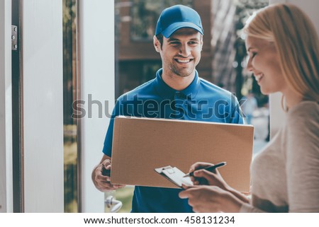 Signing to get her package. Smiling young delivery man holding a cardboard box while beautiful young woman putting signature in clipboard Royalty-Free Stock Photo #458131234