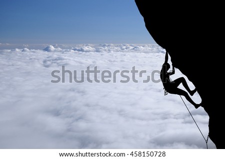 Silhouette of young woman lead climbing on overhanging cliff high above clouds and mountains, sun, beautiful colorful sky and clouds behind. Climber on top rope, hanging on rock.