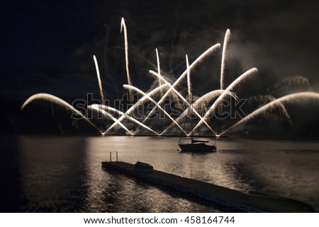 Ignis Brunensis silver and gold colored fireworks resembling aster flower reflecting on dam water surface. Long exposure night graphical photography using creative tilt effect by tilt-shift lens.