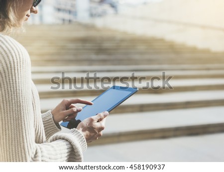 Hipster tourist texting message on tablet or technology mock up. Person using computer on building background close. Female hands holding gadget on blurred mockup. Copy space for text message, flare