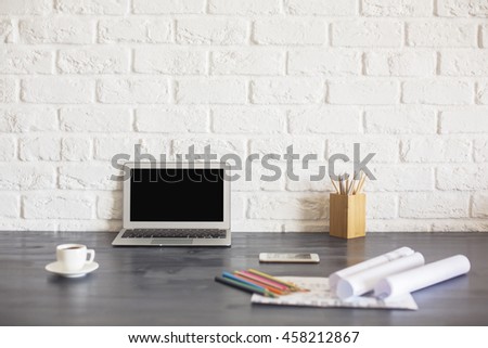 Blank laptop screen on wooden desktop with coffee cup, pencils, paperwork and other items on white brick background. Mock up
