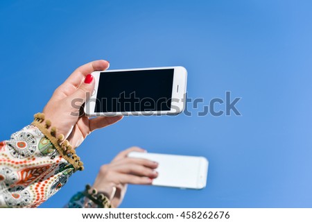 Hand holding smartphone on blue sky outdoors, reflection background. Mock up closeup view