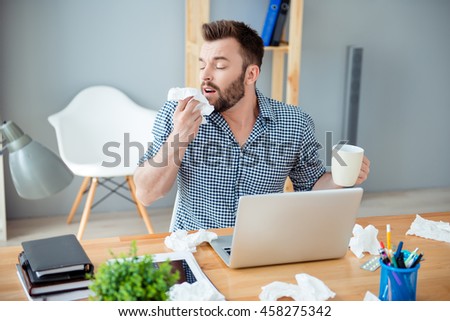 Sick businessman holding cup of hot tea and sneezing in tissue Royalty-Free Stock Photo #458275342