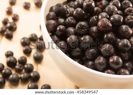 White bowl full with fresh and tasty aronia spilled on wooden table