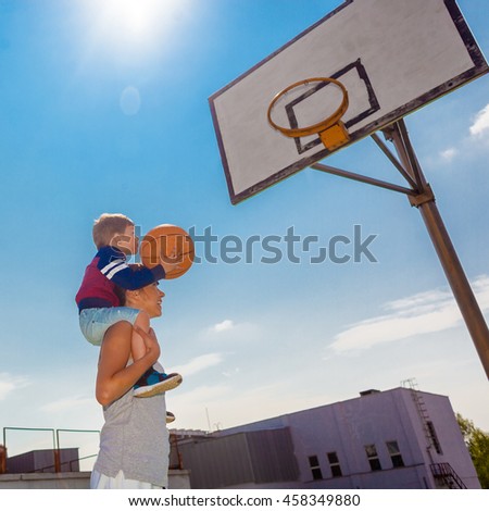 Mother carries her son on his shoulders, and playing basketball. Mom helps son to play basketball.