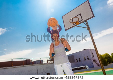 Mother carries her son on his shoulders, and playing basketball. Mom helps son to play basketball.