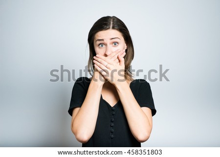 Young scared woman covering the mouth. studio photo isolated on a gray background