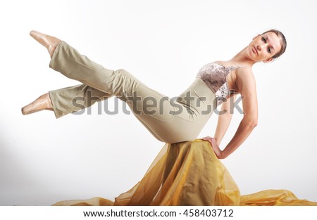 sports girl in a ballet hall in a complex ballet pose.ballerina warming up, light tones picture. daylight falls on the blonde girl