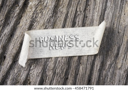 TORN paper with BUSINESS NEWS word on wooden background. GRAIN AND RUSTIC EFFECT.