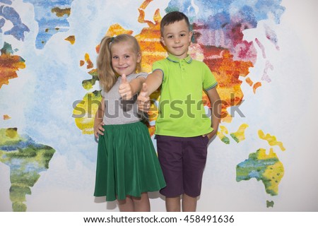 Everything will be great. Two happy young students showing their thumbs up and smiling while standing close to each other over wall painted like map of the world.