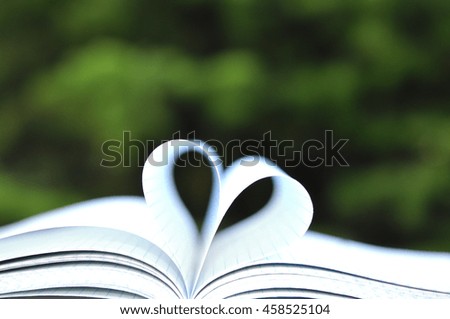 Open book with pages in heart shape on wooden table on natural background