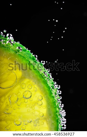 Slice of lime surrounded by water bubbles with copy space on the black background