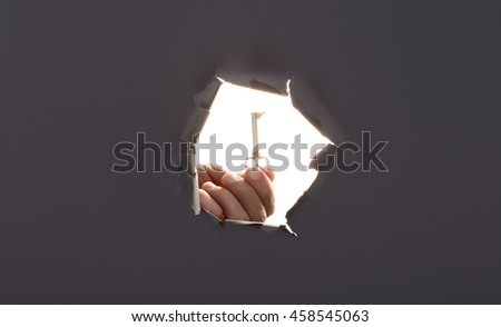 Male hand breaking through the gray paper background and holding key. High resolution.