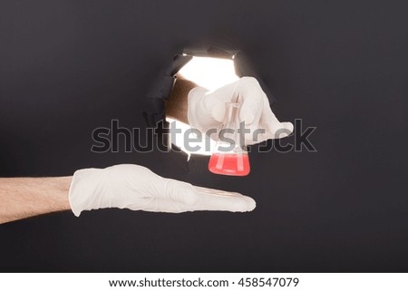 Male hand breaking through the paper background and holding test tube. High resolution.