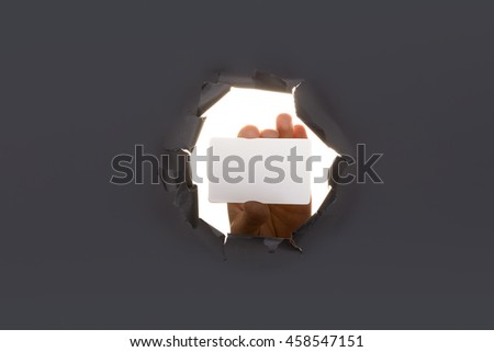 Male hand breaking through the paper background and holding bussiness card. High resolution.