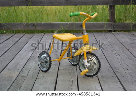 Children's three-wheeled bicycle yellow. Out on the floor of wooden planks. Close-up. Old. Peeling paint. / Children's bike / Feodor Eremin.