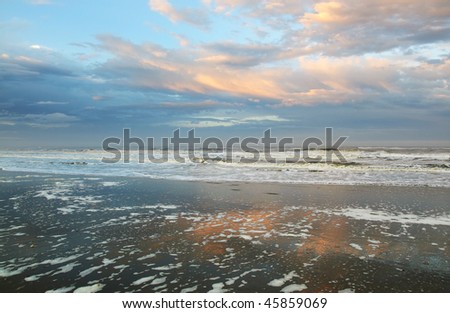 Sunset, waves, pink and blue clouds reflect on wet broad sandy seashore