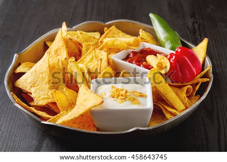 Tortilla chips on a blue plate with spicy tomato salsa. Mexican food. Dark background.