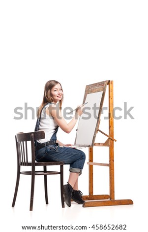Young smiling woman painter with paintbrush standing at easel 