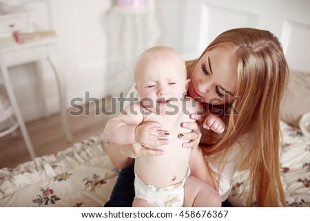 Mom with baby in bedroom. Young woman in white shirt and jeans holding her baby.