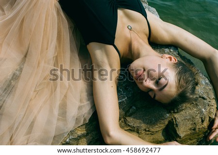 gymnast girl in a dress lying on the rocks, depicts flying ballerina dancing