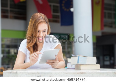 Asian women students Using a mobile phone while reading a book. on campus.
