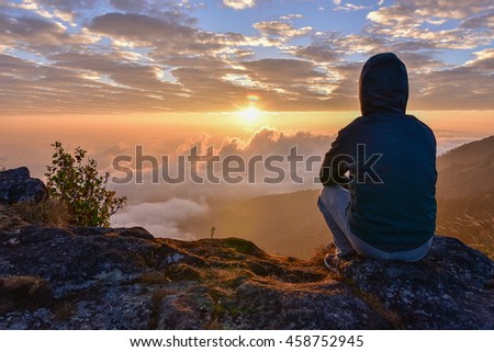Man sitting on a mountain for watching Sunrise views alone,success and peace concept. Royalty-Free Stock Photo #458752945