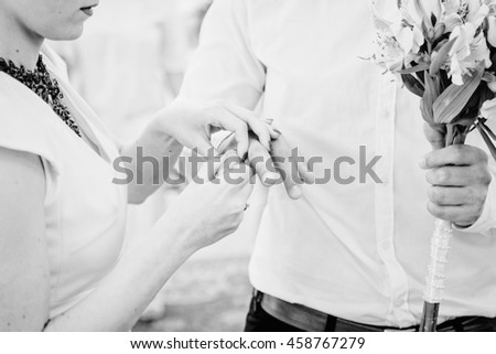 Black and white picture of bride adjusting a ring on groom's finger