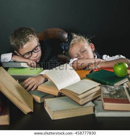 Schoolboy and schoolgirl sleeping together at the table with many books. Many homeworks or exam is stress for little kids. Motivate your child to study a boring subject. Heavy school program. Overwork