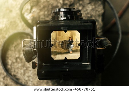 stylish happy woman in viewfinder of  analog film camera on background of city old wall