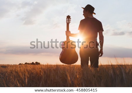 silhouette of musician with guitar at sunset field, music background Royalty-Free Stock Photo #458805415