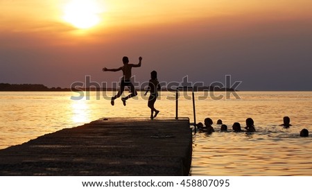 Summer in Croatia. Silhouettes of kids having fun on the pier at sunset - Playing, swimming and jumping in the water.