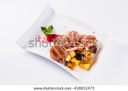 rack of lamb with potatoes and eggplant on a white plate on a light background