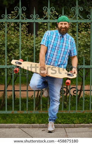 Smiling hipster man posing with longboard and on fashionable green cap.