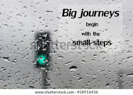 Word  Big journeys begin with the small steps.Inspirational motivational quote on traffic light on a rainy day window background 