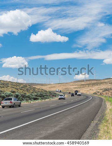 Interstate Highway I90 and row of wind turbines of windfarm in Ellensburg, Washington, US. Windmills again blue cloud sky. Clean, sustainable, renewable energy. Transportation, electricity background.