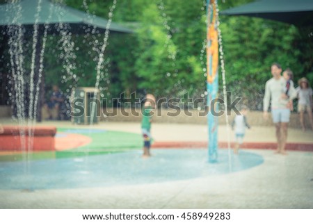 Blurred motion of kids having fun play with water at playground in summer time. Activities for children and family at urban outdoor aquatic park with water sprinkles and fountain. Vintage filter look.